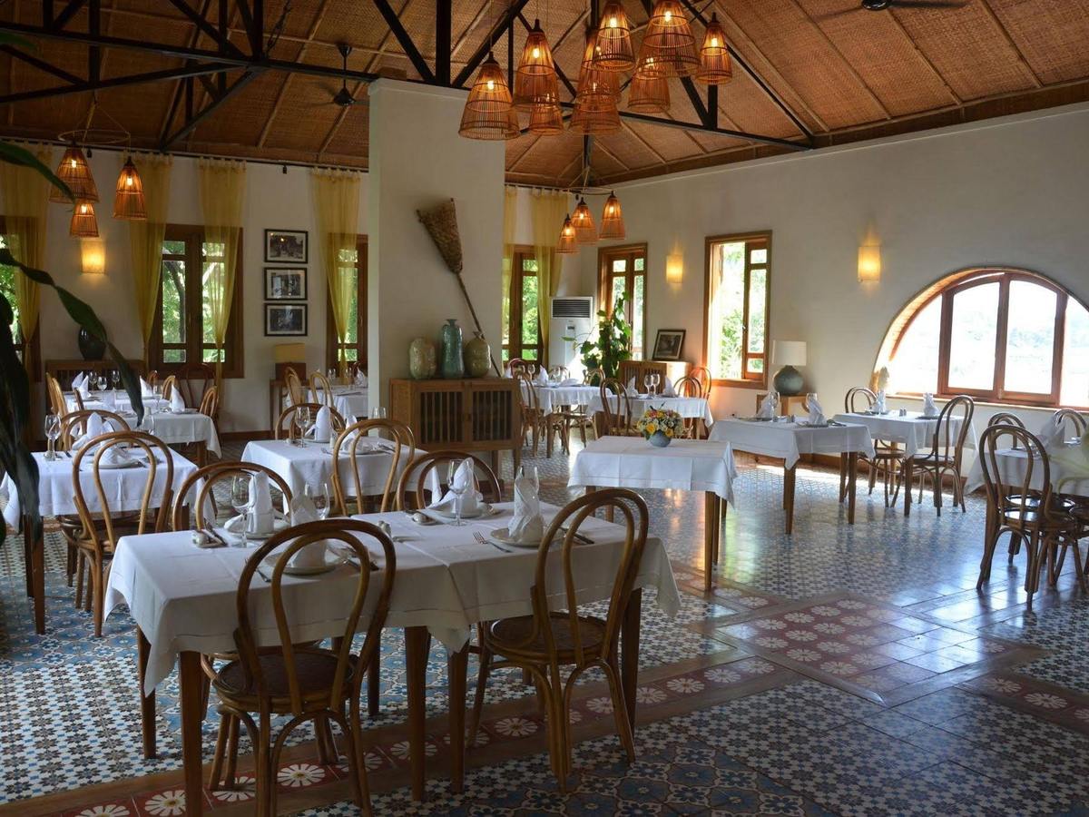 Dining room with white tablecloths, bentwood chairs, cement-tile floor and arched windows onto greenery