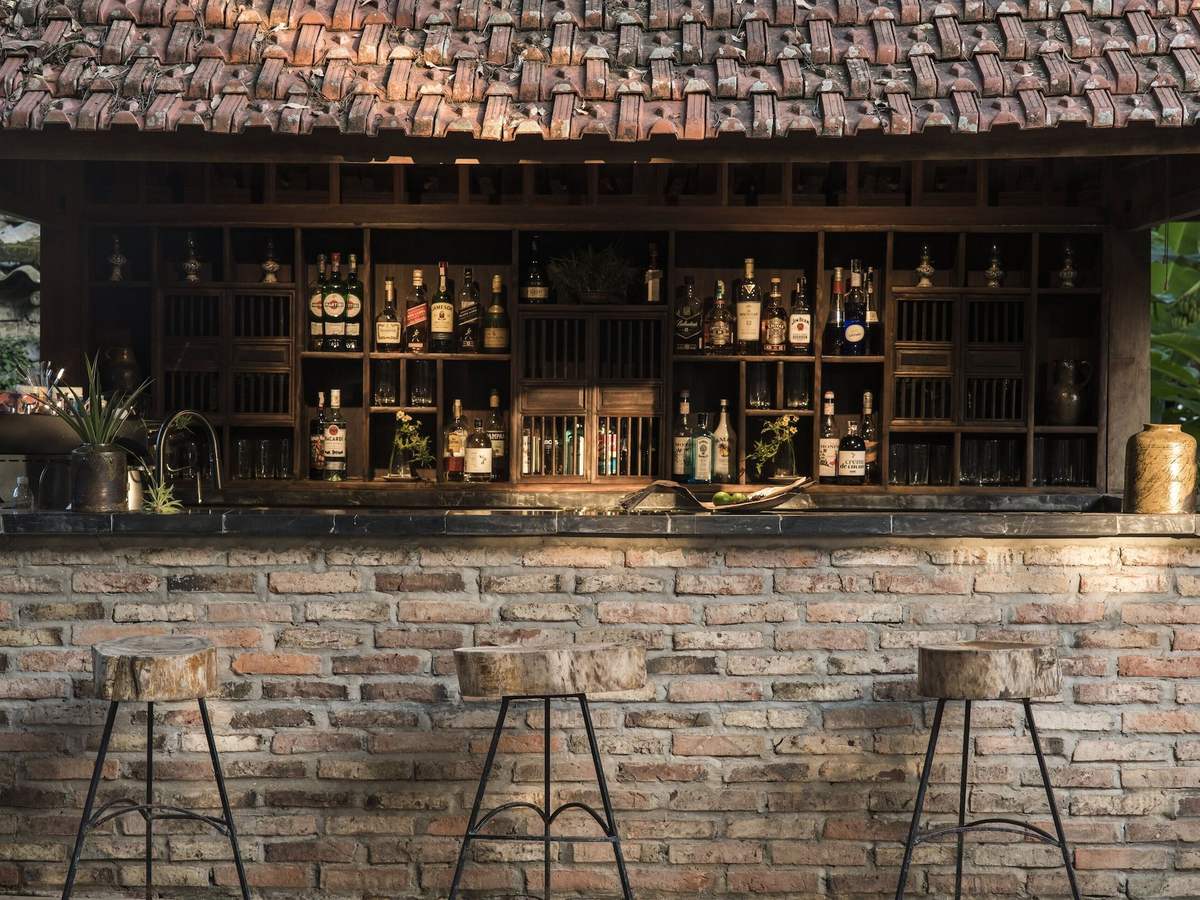 Garden bar with a brick counter, bar stools and shelves of bottles under a tiled roof