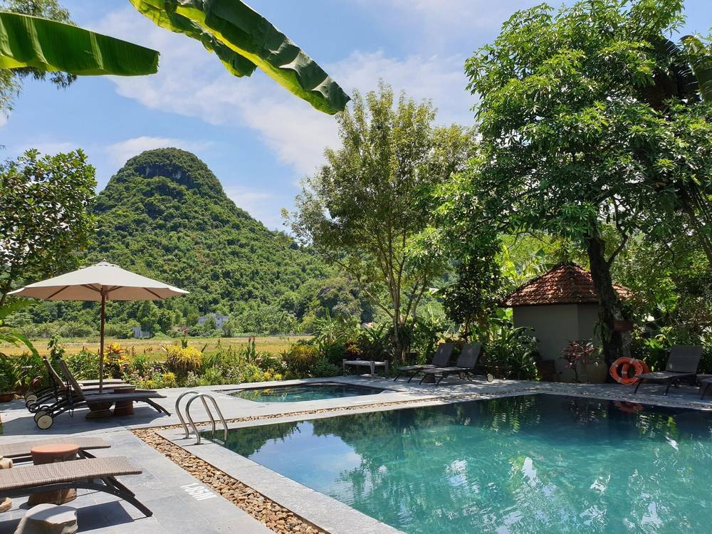 Outdoor pool with sun loungers and a parasol, a rounded limestone peak and rice fields behind the garden
