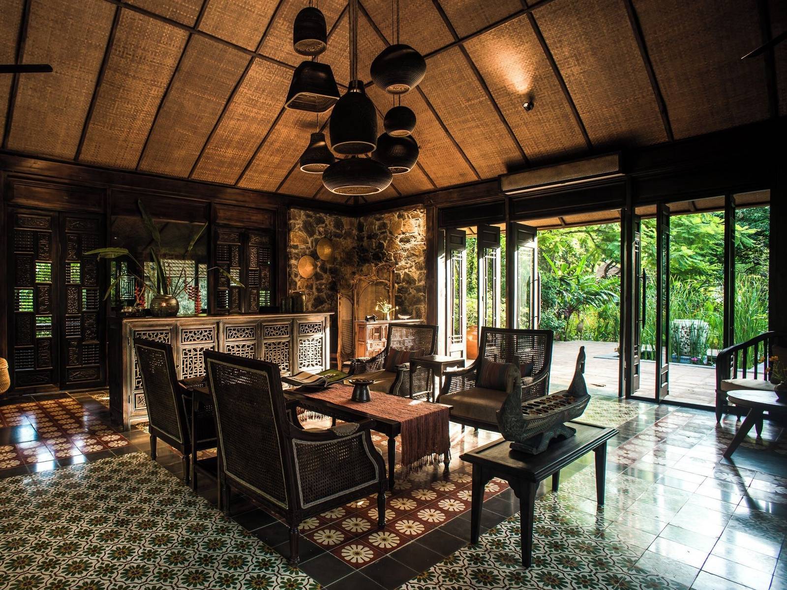 Lobby lounge with carved wooden chairs, a long table, cement-tile floor and glass doors open to the garden