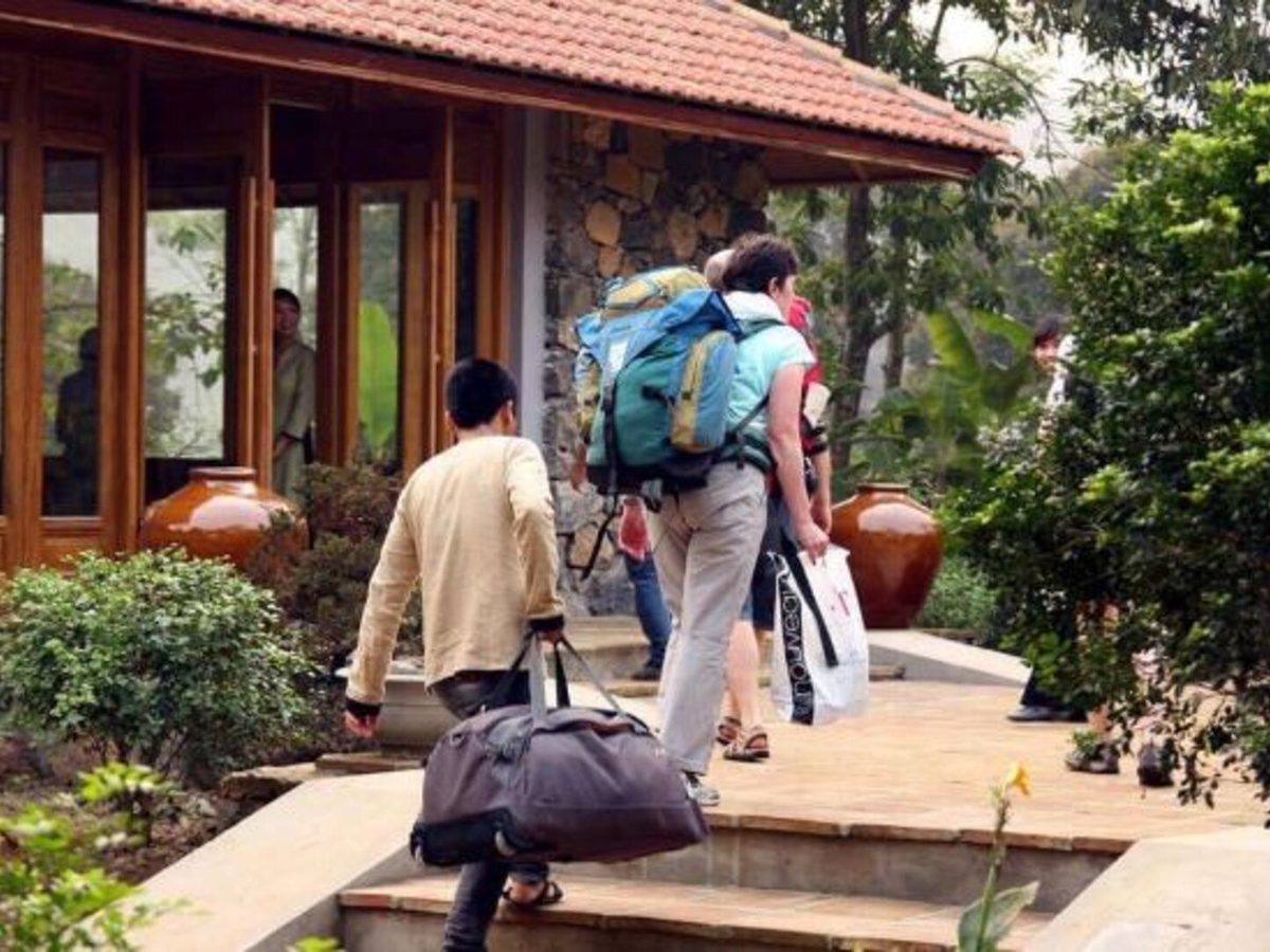Guests with backpacks and a suitcase walking up a paved garden path toward a timber-framed reception