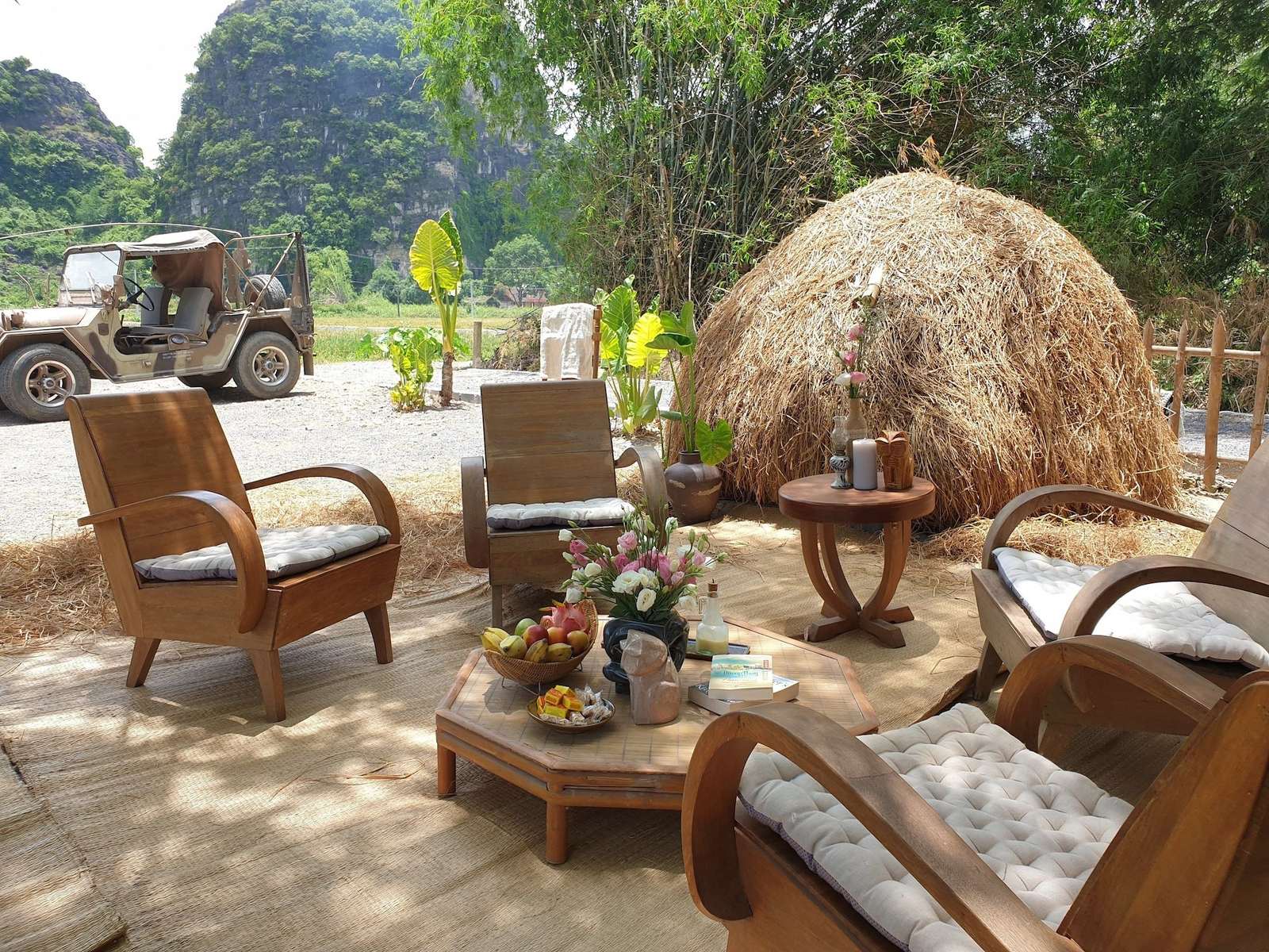 Wooden lounge chairs beside a haystack on a garden terrace, with an old jeep and limestone peaks behind