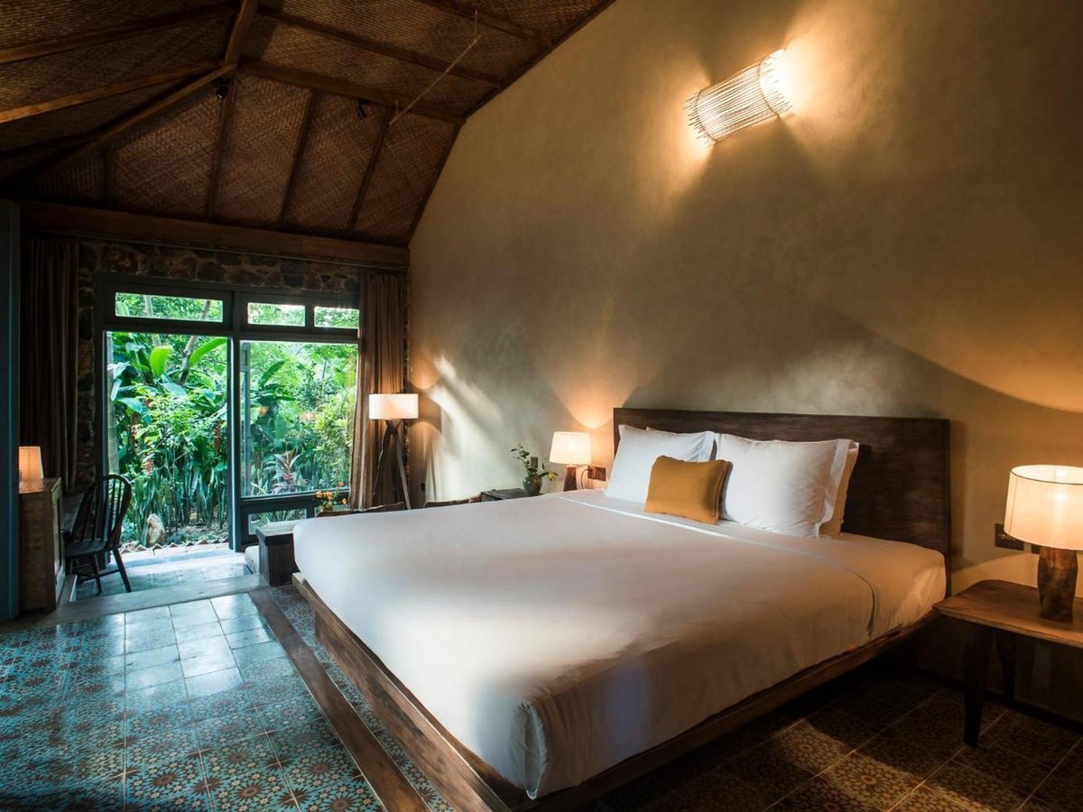 Bungalow bedroom with a pitched woven ceiling, wall lamps, patterned floor tiles and glass doors to the garden