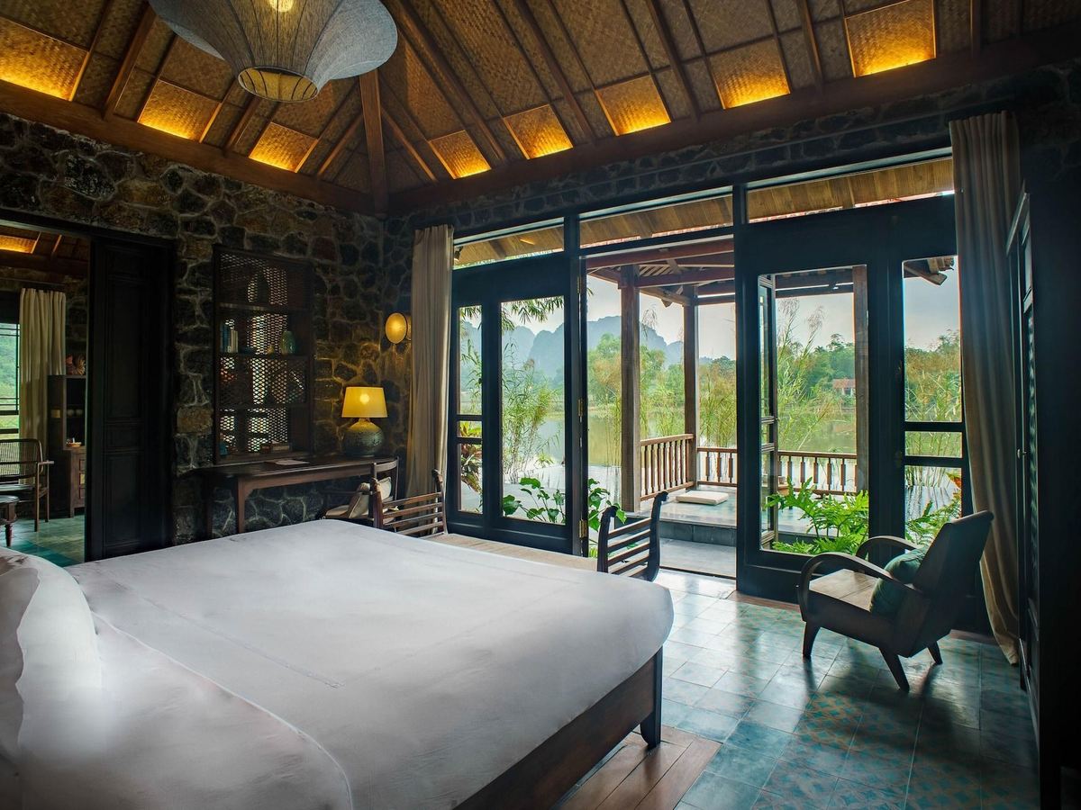 Villa bedroom with a dark timber ceiling and floor-to-ceiling glass doors opening onto a deck and the garden