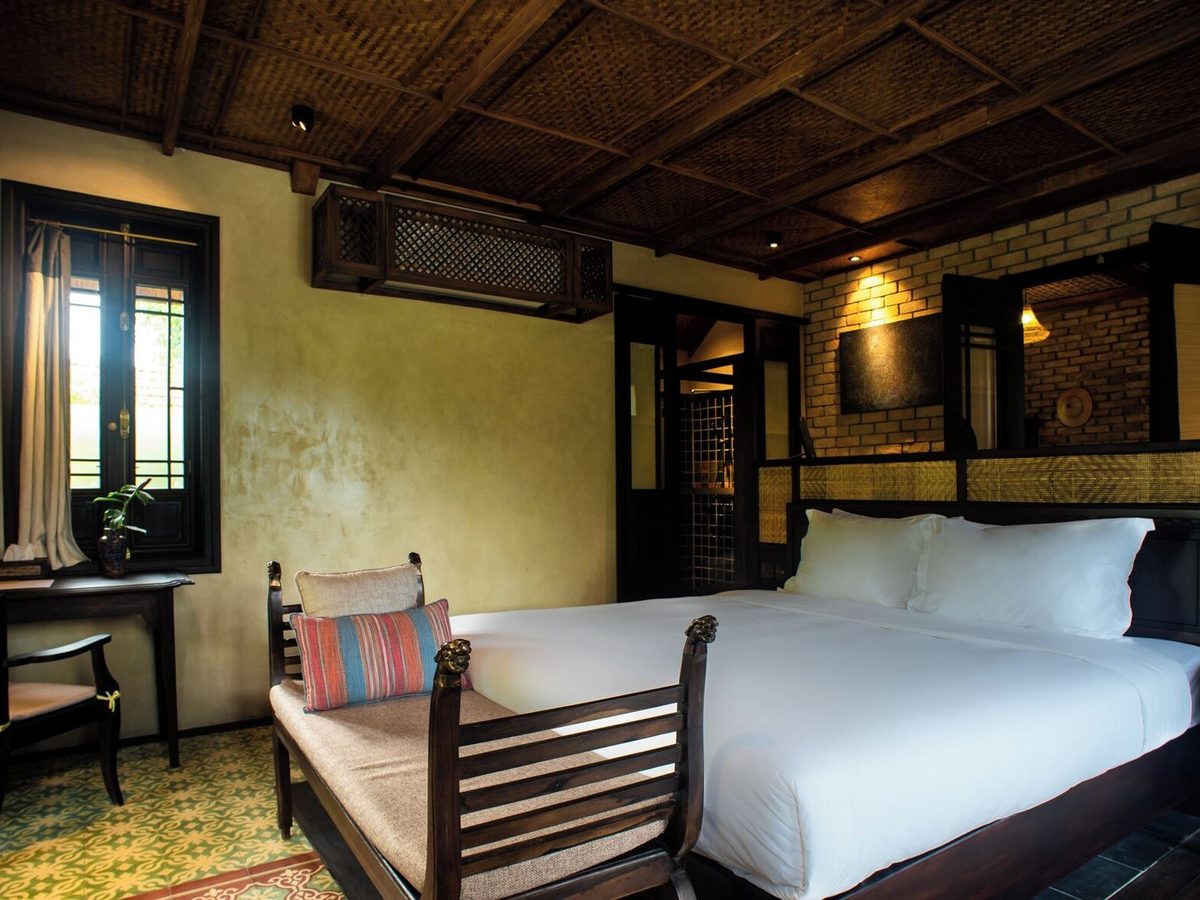 Chamber with a king bed, a wooden bench at its foot, an armchair and tall shuttered windows
