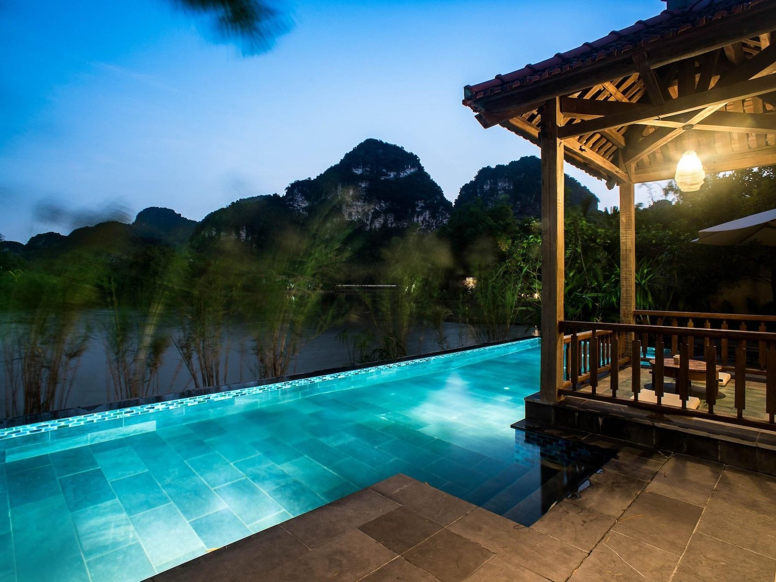 Turquoise private pool beside a timber pavilion at dusk, with limestone peaks dark against the evening sky