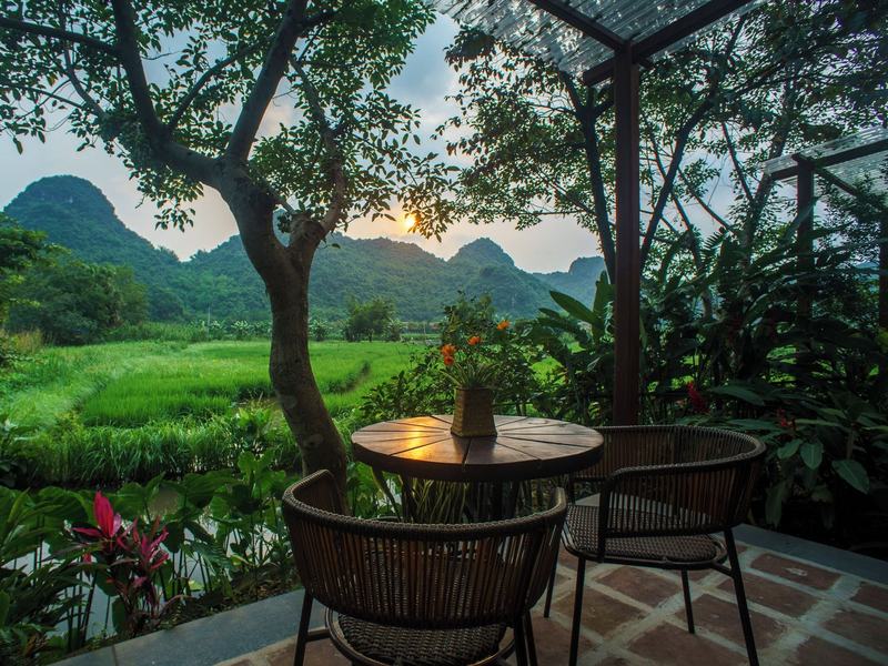 A terrace table and rattan chairs looking out over green rice fields to a line of limestone peaks